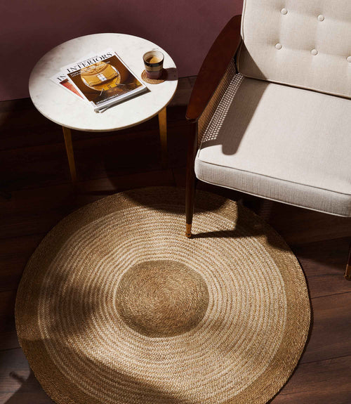 Round jute rug beside armchair and marble side table.