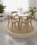 Round dining table with four wooden chairs on a jute rug in a bright room with plants.