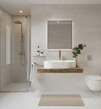 A white, oval-shaped vessel sink sits atop a floating wooden shelf. Above the sink is a large, rectangular mirror with backlighting. A gold-toned faucet and some small toiletries are visible.