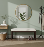 a well-decorated entryway or hallway area with a light green wall. Key items include a round gold-framed mirror hanging above a dark wood bench with a white cushion. 