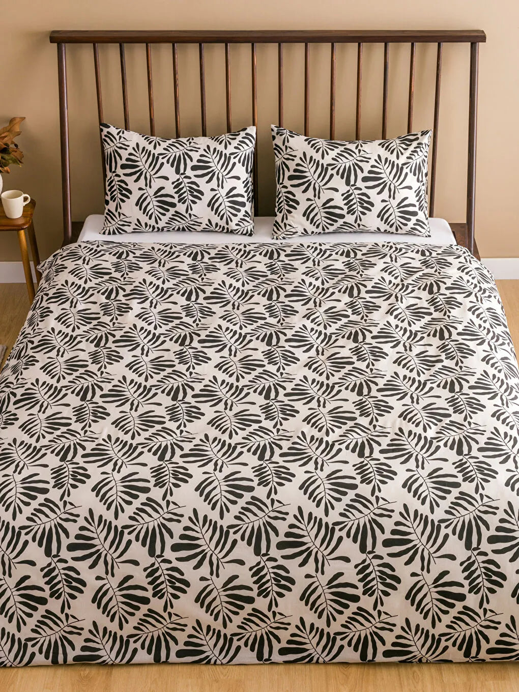 Bed with black and white leaf patterned duvet cover and pillows against a beige wall.
