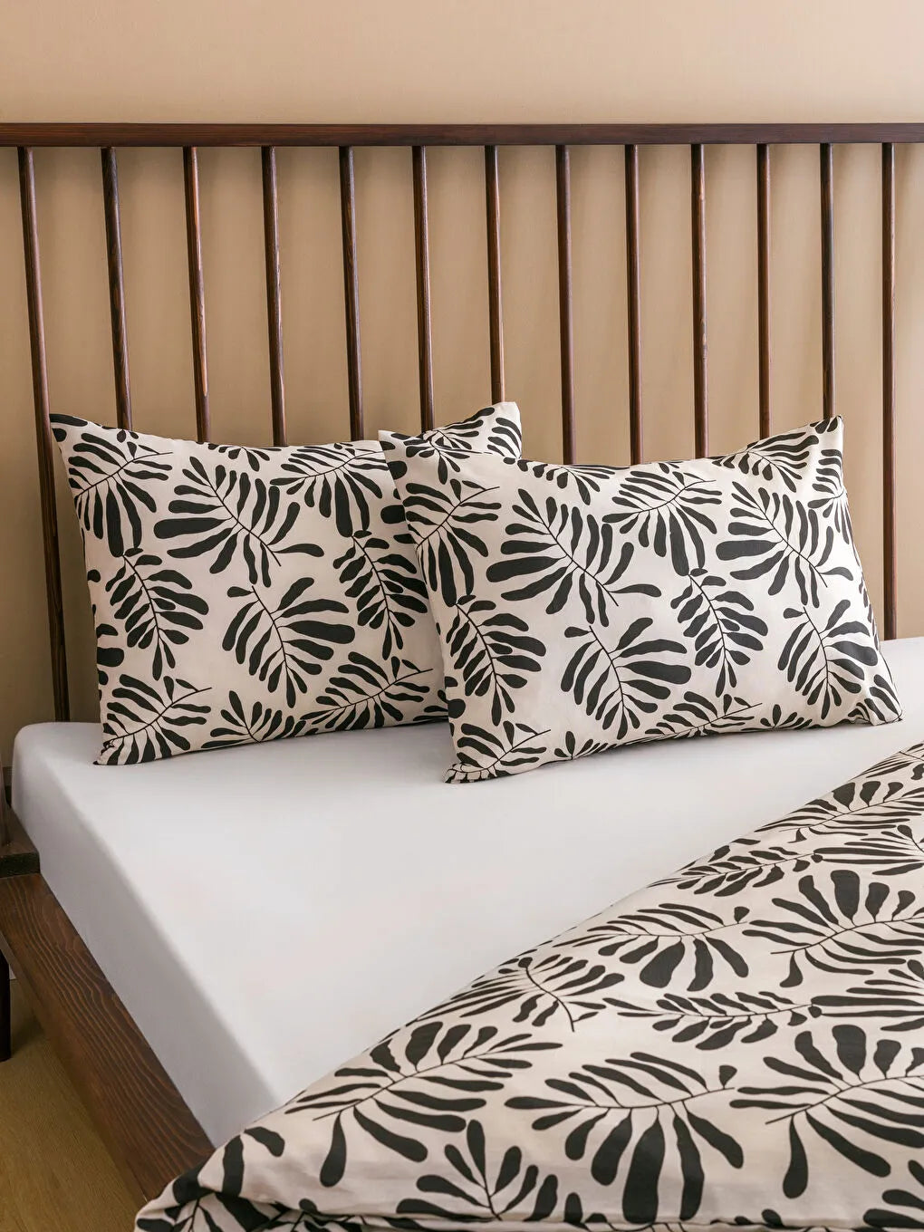Bed with leaf-patterned pillows and bedding against a wooden headboard.