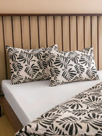 Bed with leaf-patterned pillows and bedding against a wooden headboard.